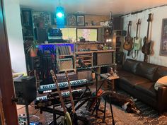 a living room filled with lots of musical equipment and guitars on the wall behind it