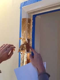 someone is painting the outside of a door with blue tape and gold foil on it