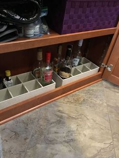 an open cabinet filled with liquor bottles and empty glasses on the floor in front of it