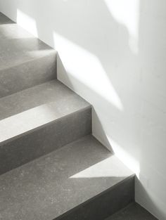 the shadow of a person walking up some stairs in front of a white wall and floor