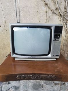 an old tv sitting on top of a wooden table next to a wall with vines