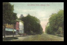 an old photo of a street with buildings and trees on both sides, surrounded by grass