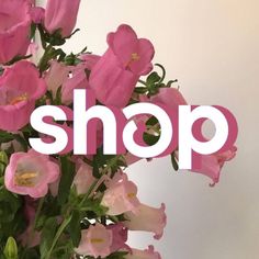 a vase filled with pink flowers sitting on top of a white table next to a sign that says shop