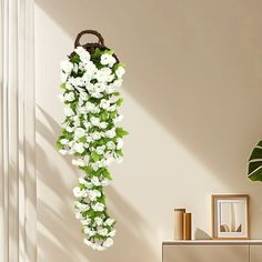 white flowers hanging from the side of a wall next to a dresser and potted plant