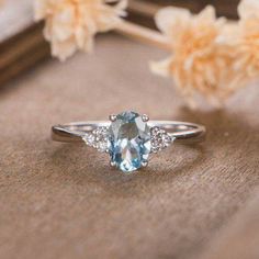 an oval cut aqua blue topazte and diamond ring on a table with flowers in the background