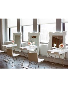 four white chairs with flower vases on them in front of a mirror and window