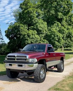 a large red truck parked on top of a dirt road next to trees and grass