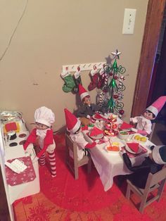 two elfs sitting at a table in front of a christmas tree and other decorations