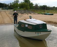 a man standing next to a small boat in the water on a sandy shore line