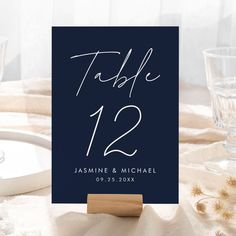 a table number card on top of a wooden stand next to two glasses and plates