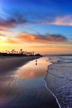 the sun is setting at the beach with people walking in the water and on the sand