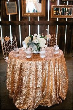 a gold sequin table cloth with white flowers and candles on it for a wedding reception