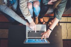 four people sitting at a table with their hands on the keyboard of an open laptop