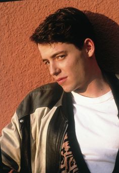 a young man leaning against a wall wearing a leather jacket