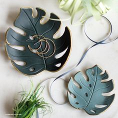 two green and gold plates sitting on top of a white table next to a plant