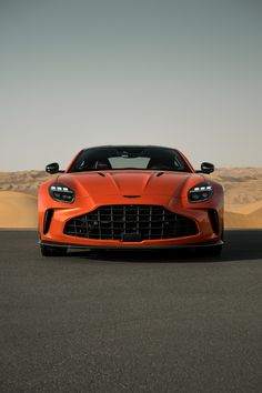 an orange sports car parked in front of a sand dune with its hood up and headlight on