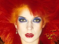 a woman with bright red hair and blue eyeshadow is posing for the camera