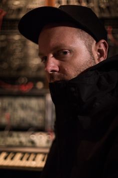 a man wearing a black hat and jacket in front of an organ keyboard with other musical equipment behind him