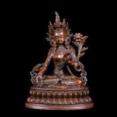 a bronze buddha statue sitting on top of a wooden table next to a black background