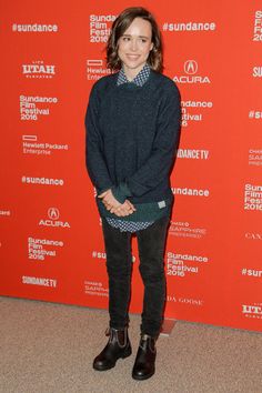 a woman standing in front of a red wall wearing black boots and a blue sweater