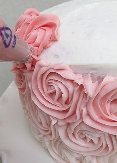 someone is decorating a cake with pink icing