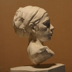 a sculpture of a woman's head is shown on a white pedestal in front of a brown wall