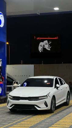 two white cars are parked in front of a gas station with an advertisement on the wall