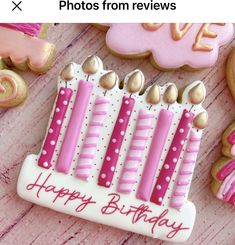 pink and white decorated birthday cake cookies on wooden table with cookie cutters next to it