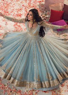 a woman in a blue and gold dress standing on a bed with flowers all around her