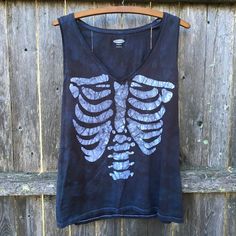 a black shirt with white skeleton on it hanging from a wooden hanger next to a fence