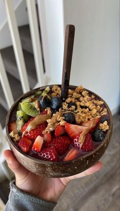 a person holding up a bowl of fruit and granola