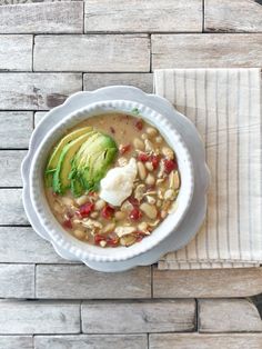 a white bowl filled with soup and topped with avocado on top of a wooden table