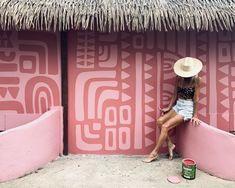 a woman in a straw hat leaning against a pink wall