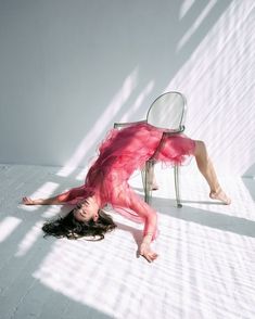 a woman in a pink dress laying on the ground next to a chair and looking up