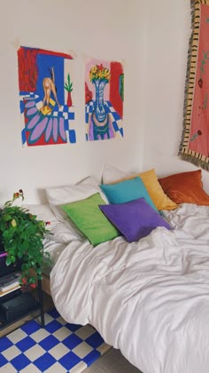 a bed with white sheets and colorful pillows on it next to a potted plant