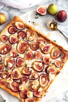 a square pizza with figs and cheese on it next to other fruit, including apples