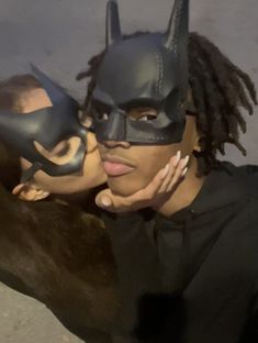 a woman wearing a batman mask and holding her face up to the camera with another person in front of her