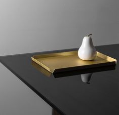 a white pear sitting on top of a black table next to a gold tray with a mirror