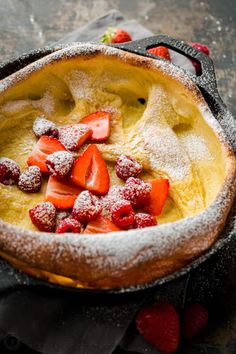 a bowl filled with fruit and powdered sugar on top of a black cloth next to strawberries