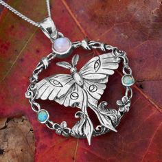 Anyone who has witnessed the haunting beauty of a live luna moth will understand the magic of this sterling silver tribute. This pendant has been lovingly sculpted and beautifully detailed, right down to the feathery antennae and delicate eyespots on the wings. A ring of vines and flowers surrounds the moth, forming an exquisite backdrop for a trio of genuine gemstones: a pair of green opals under the wings, and at the top, a magnificent rainbow moonstone. There is just so much to love about thi Spiritual Nickel-free Moon Shaped Jewelry, Lunar Moth Necklace, Pagan Cross Stitch, Vines And Flowers, Spiritual Moon-shaped Collectible Jewelry, Nickel-free Moon Shaped Spiritual Necklace, Haunting Beauty, Celtic Cross Stitch, Moth Pendant