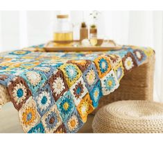 a crocheted tablecloth with multicolored squares on it and a basket next to it