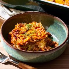 a bowl filled with food on top of a wooden table next to a pan of casserole