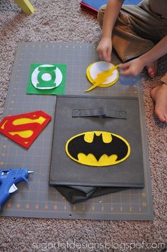 a young boy sitting on the floor cutting out paper batman and super hero logos with scissors