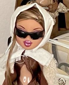 a close up of a doll wearing sunglasses and a dress with a hood over her head