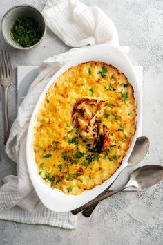 a casserole dish with chicken and cheese in it on a white cloth next to silverware