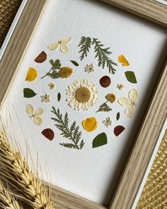 an art work with flowers and leaves in a wooden frame next to some wheat stalks