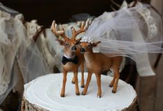 two deer figurines are standing on top of a tree stump with veils