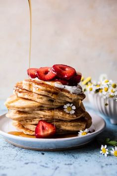 a stack of pancakes with strawberries and syrup being poured onto them on a plate