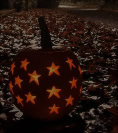 a pumpkin with stars carved into it sitting in the middle of leafy ground at night