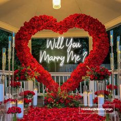 a heart - shaped arrangement with roses and candles in front of a sign that says will you marry me?